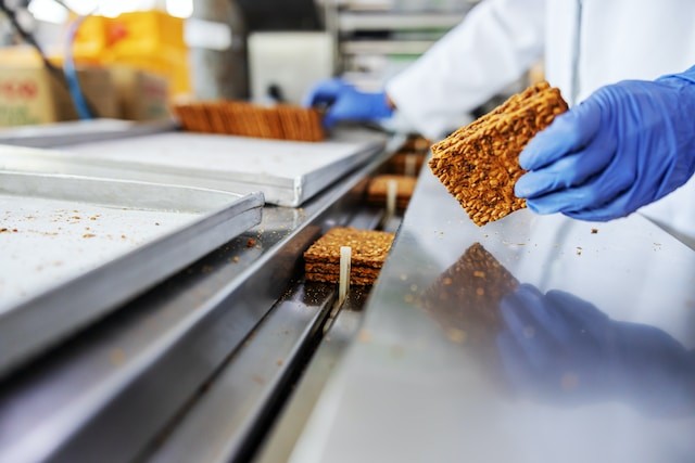 closeup-of-worker-picking-up-biscuits-form-machine-while-standing-in-food-factory